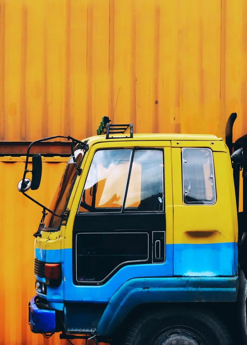 Yellow and blue cargo truck parked in front of an orange shipping container